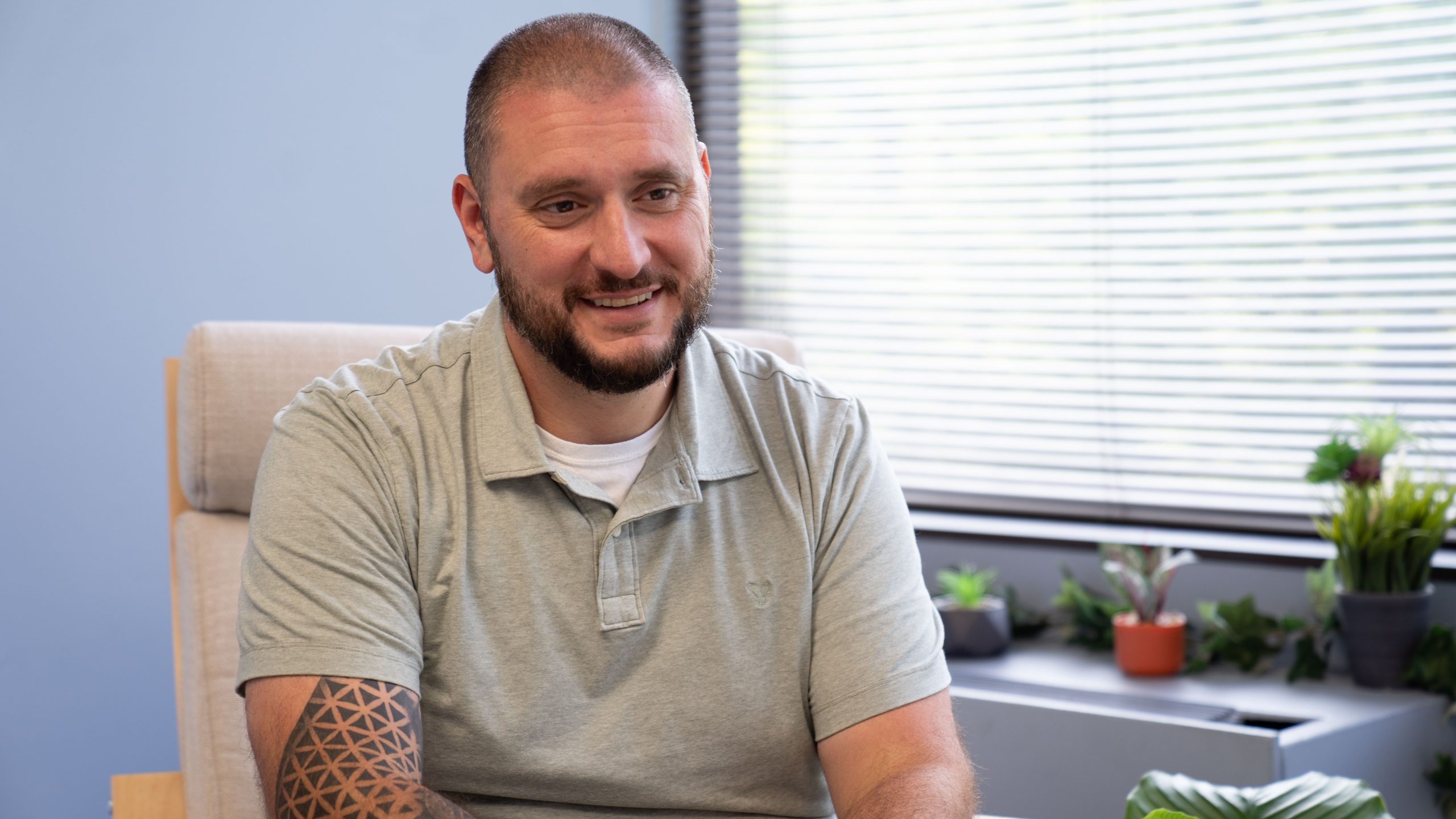 Young white man with tattoos sitting on a chair in an office