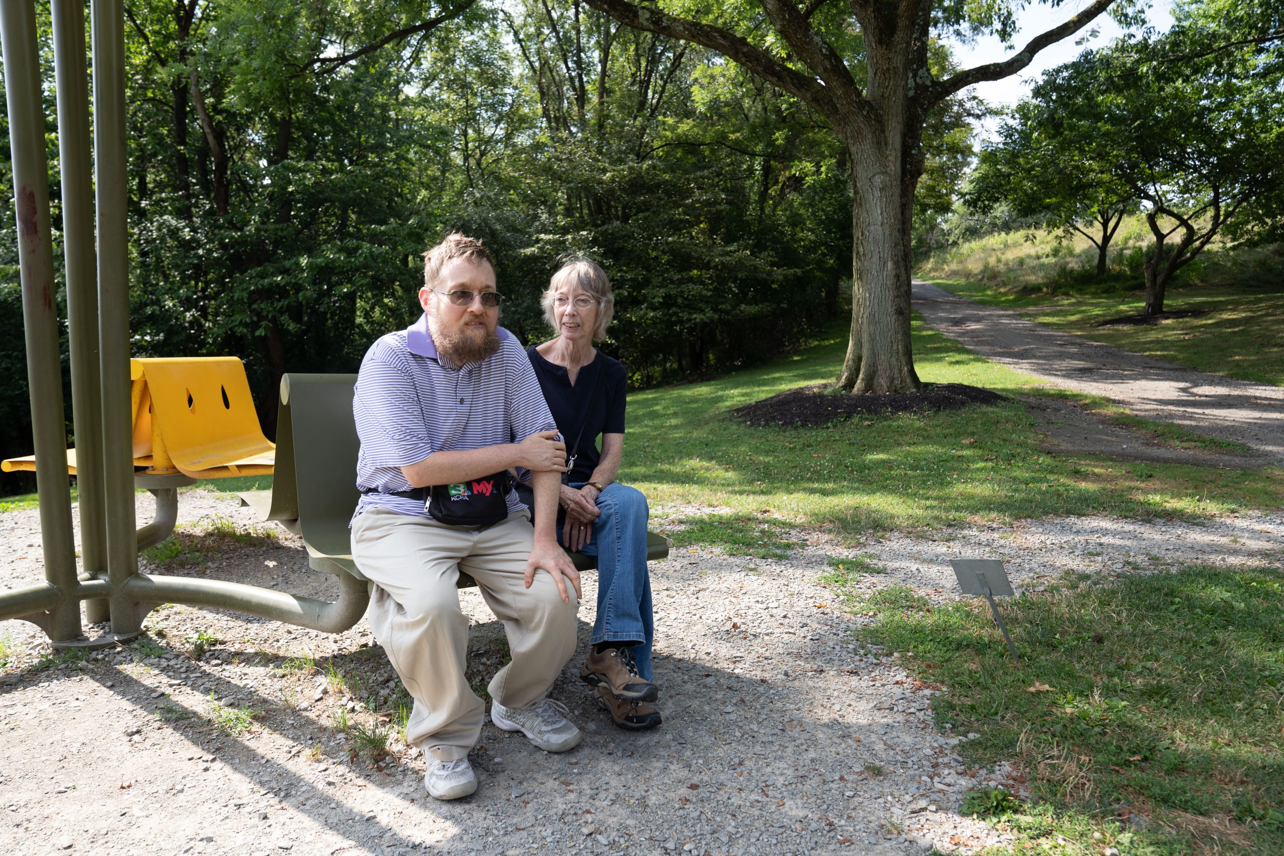 A young man with PWS and his mother on a park bench smiling