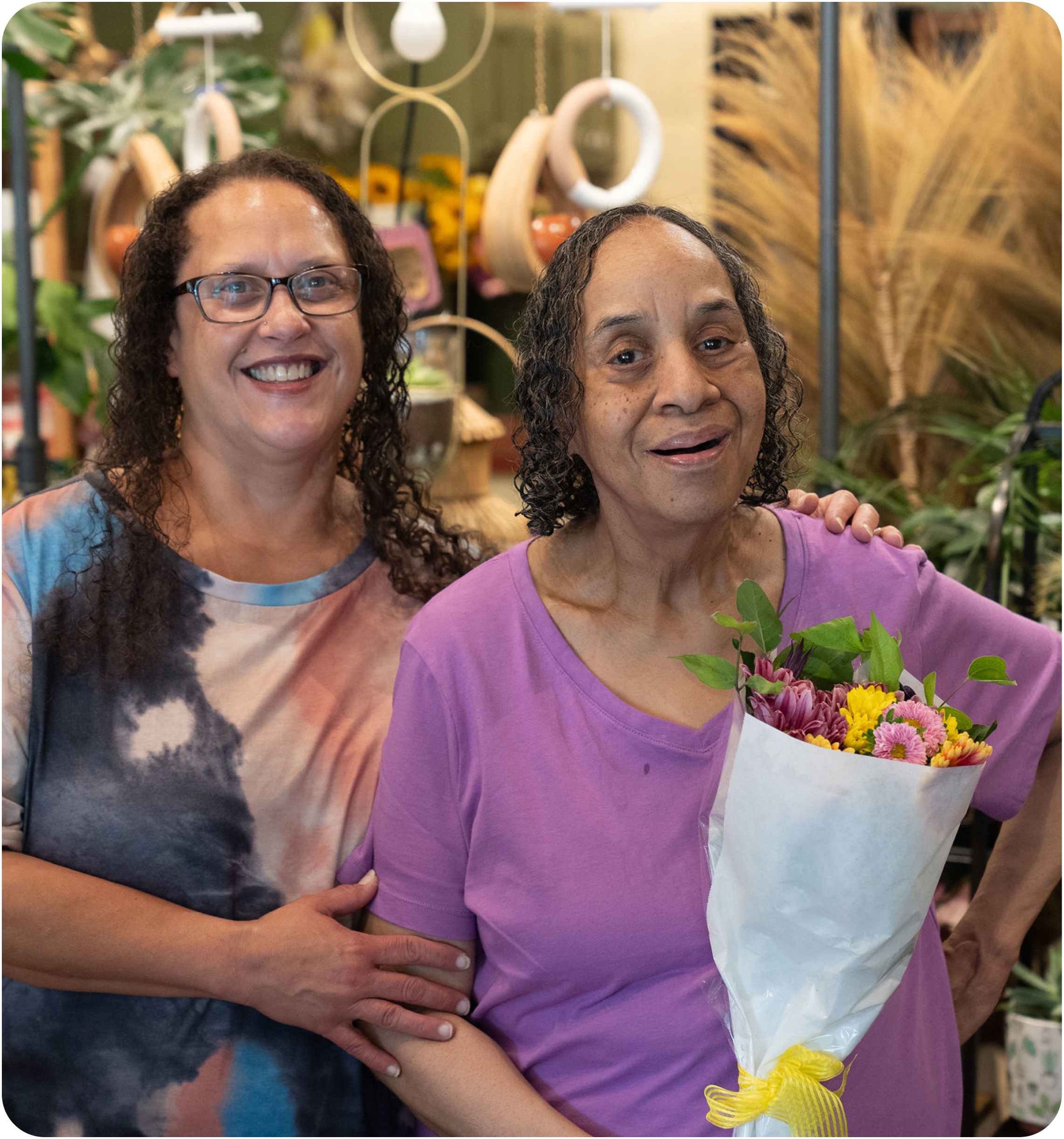 Two women smiling at the camera while holding a bouquet of flowers