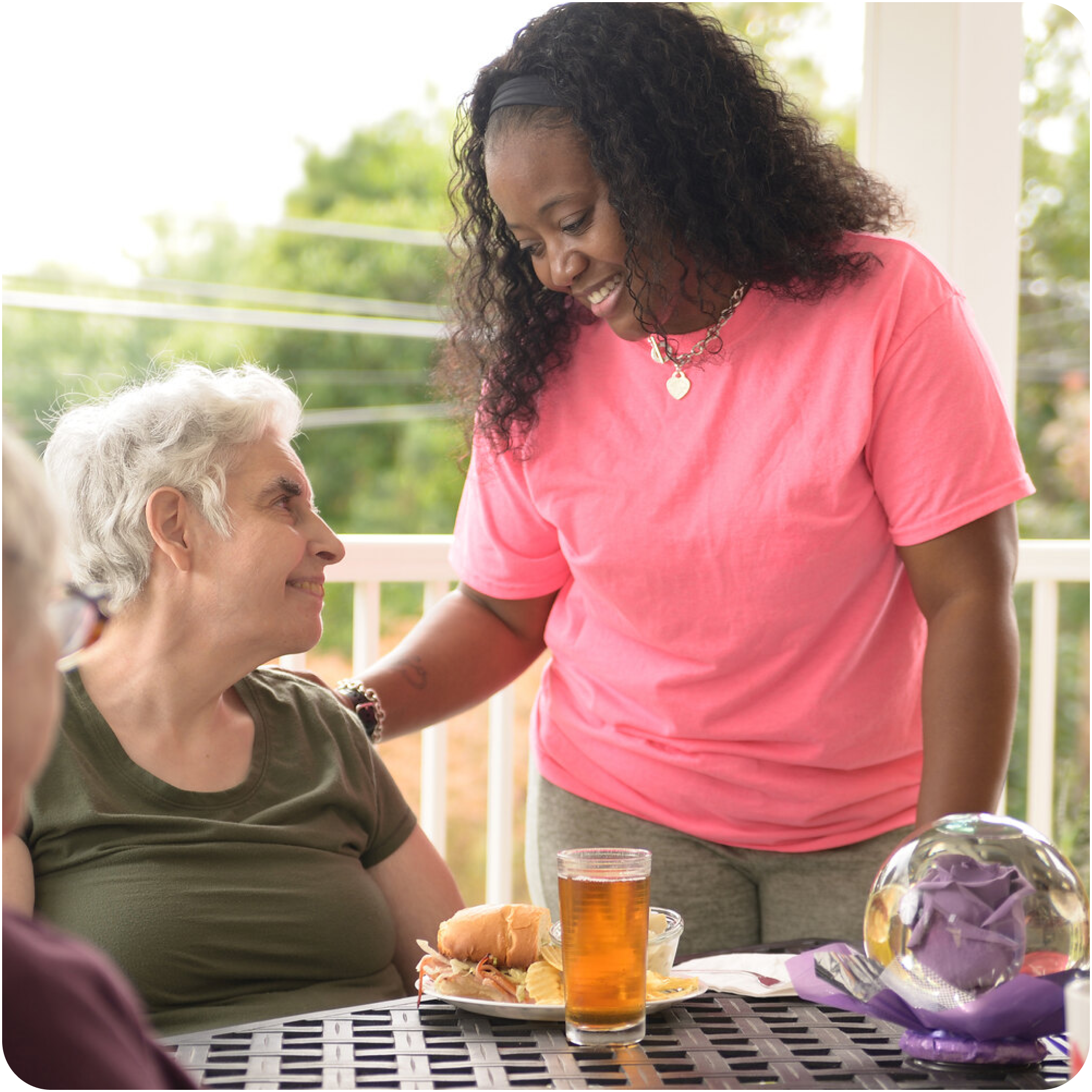 A woman serving a sandwich, chips, and iced tea to a elderly woman.