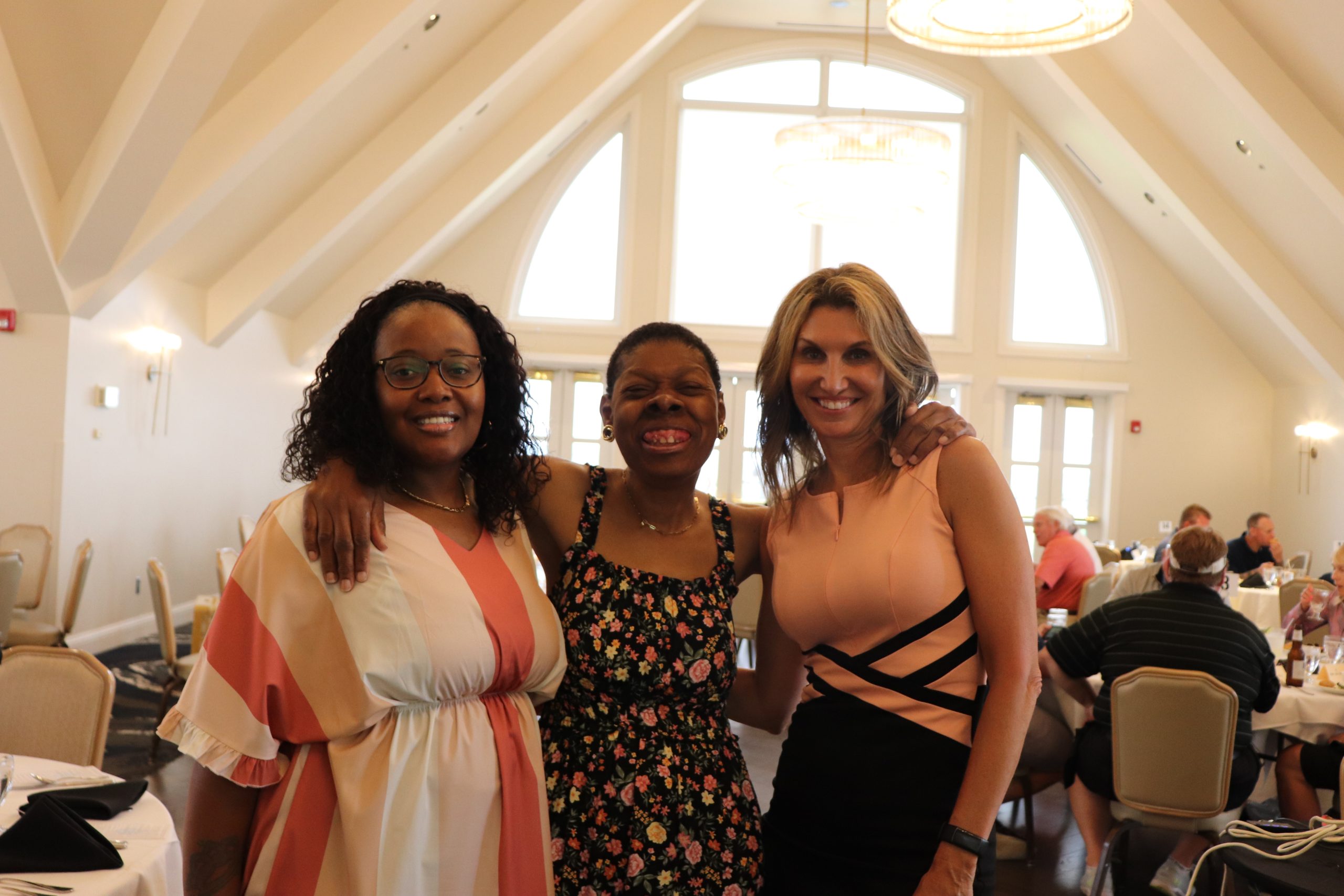 Three women pose with smiles on their faces at an event.