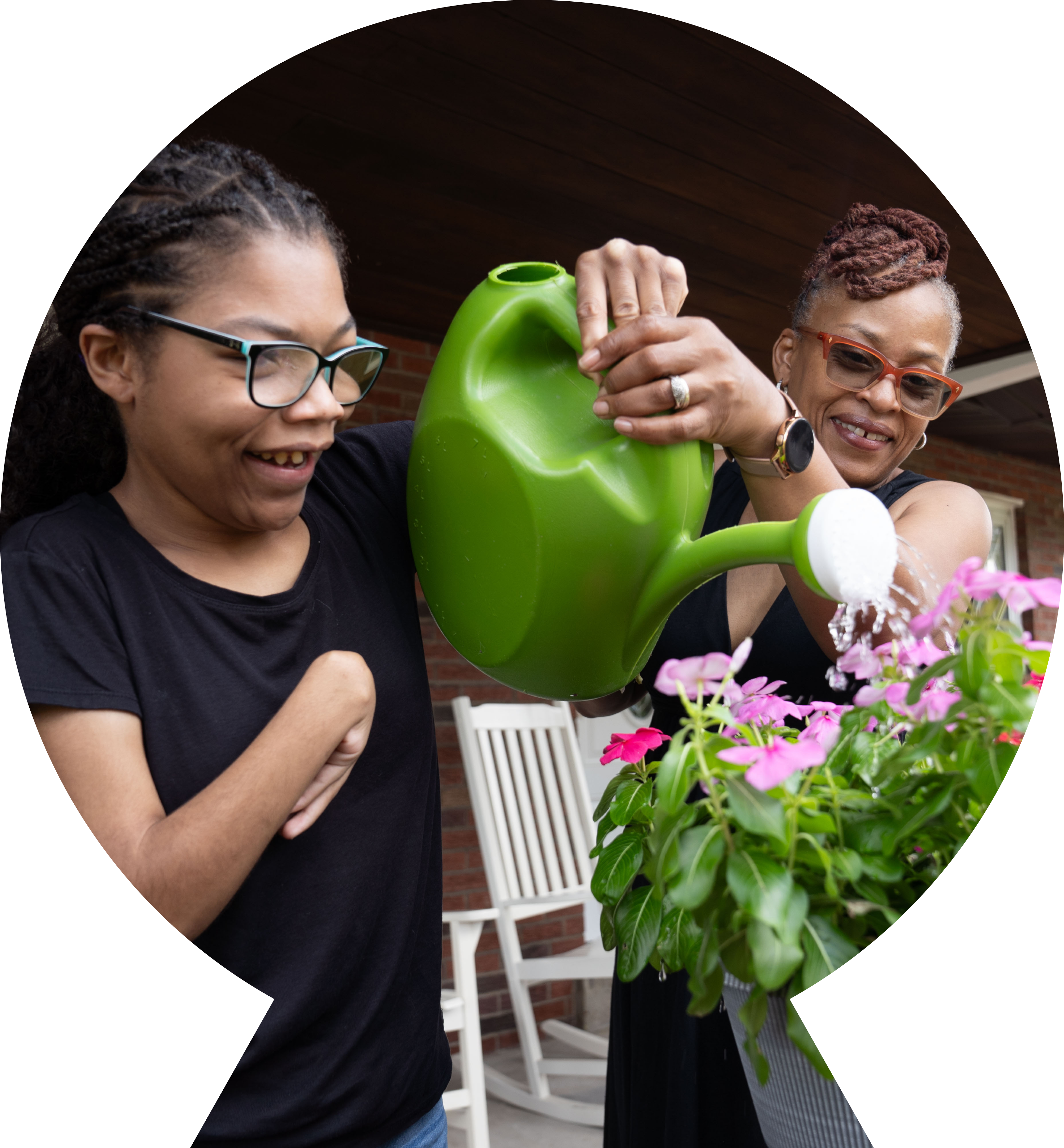 Daughter and mother watering pink flowers on a front porch with a green watering can. 